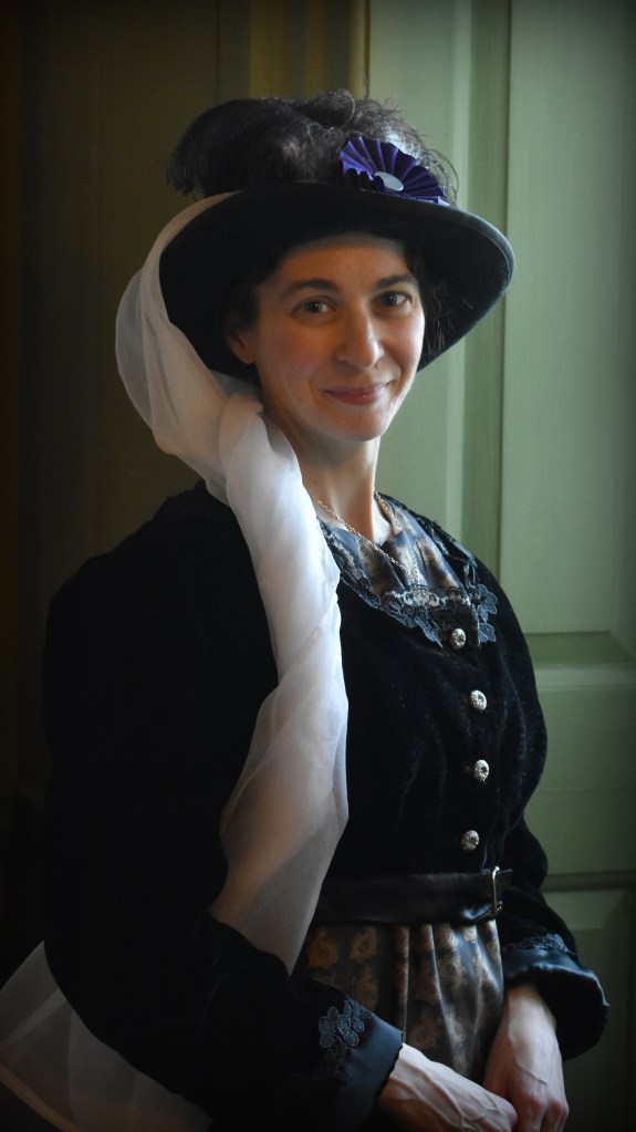 Julie Butters as Fanny Dashwood, wearing a dark hat with white veil and black velvet spencer